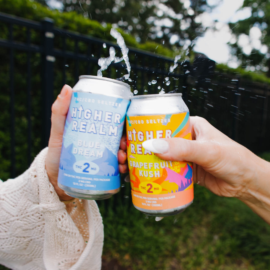 Hands cheers two cans of Higher Realm THC-infused sparkling seltzer in Grapefruit Kush and Blue Dream flavors. Lifestyle image showcasing hemp-derived THC beverages for social gatherings and relaxation.
